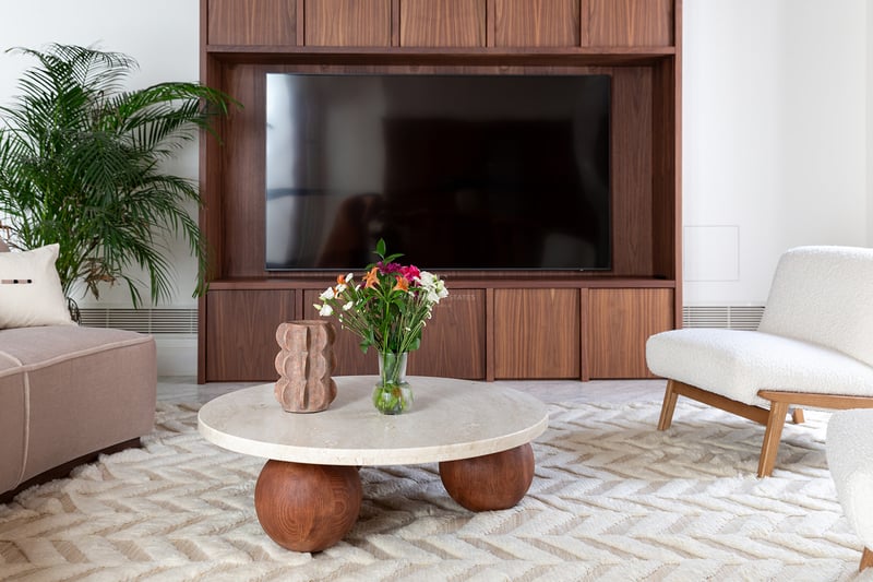 Salón contemporáneo con mueble de TV en nogal, mesa de centro redonda de travertino y sillón de bouclé blanco.