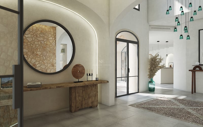 Entrada de villa con arcos, pared de piedra natural, espejo circular y consola de madera tallada.