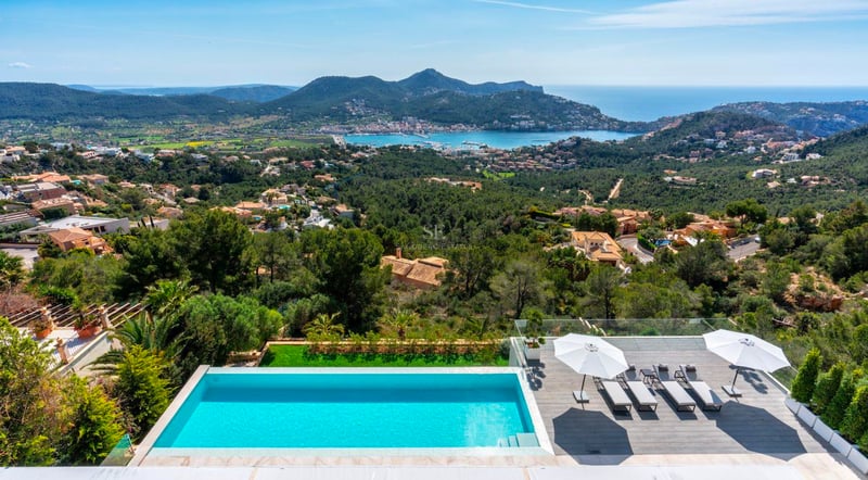 Une piscine à débordement et une terrasse ensoleillée surplombant une vallée et une baie méditerranéenne.