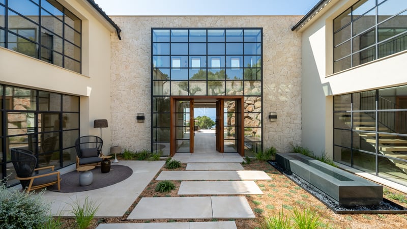 Entrée principale d'une villa de luxe avec murs en pierre, grandes baies vitrées et porte pivotante en bois massif.