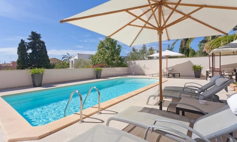 Piscine turquoise entourée d'une terrasse en pierre avec bains de soleil et parasols blancs.