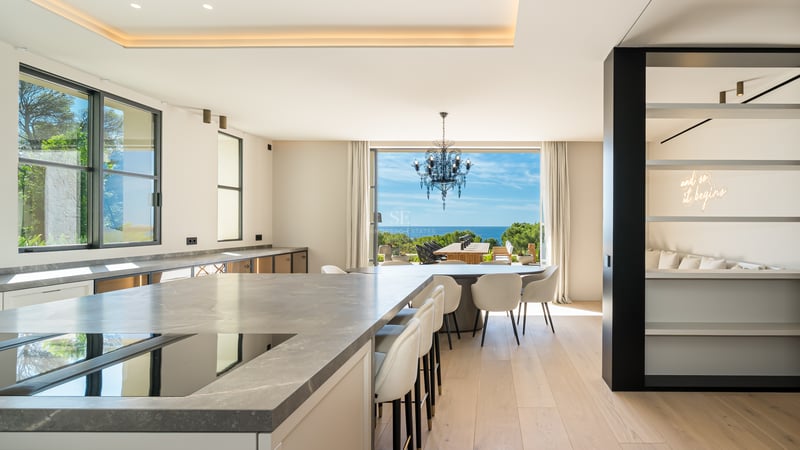 Cuisine haut de gamme avec îlot en marbre et salle à manger surplombant la Méditerranée par de grandes baies vitrées.