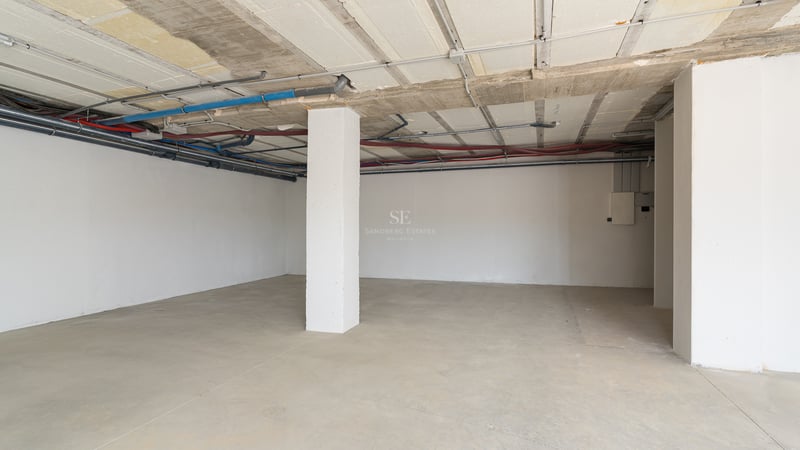 Grand parking souterrain en béton avec tuyauterie apparente et une colonne de soutien blanche.