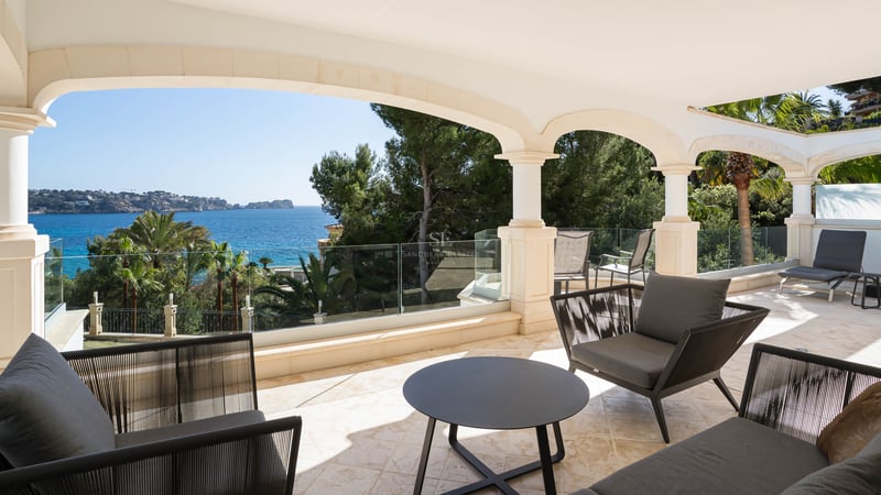 Terrasse couverte en pierre avec arches, garde-corps en verre et mobilier moderne surplombant la Méditerranée.