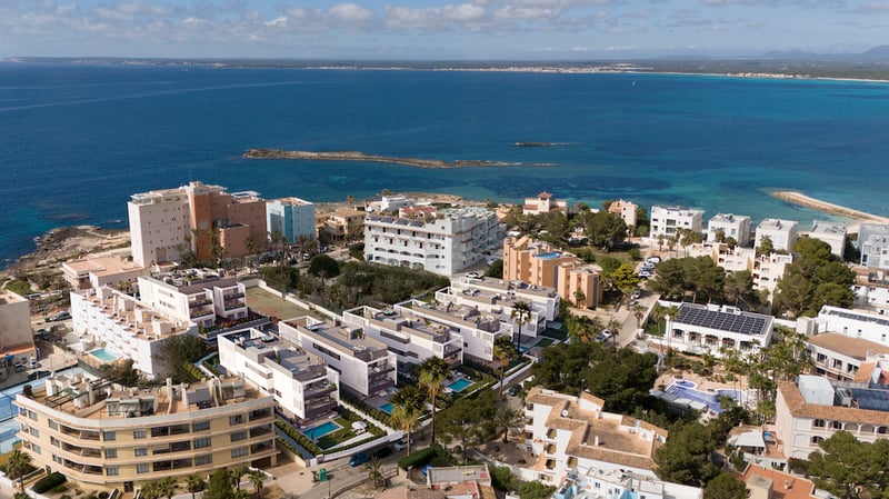 Vista aérea de modernos edificios blancos frente al mar azul con piscinas privadas y jardines en Mallorca.