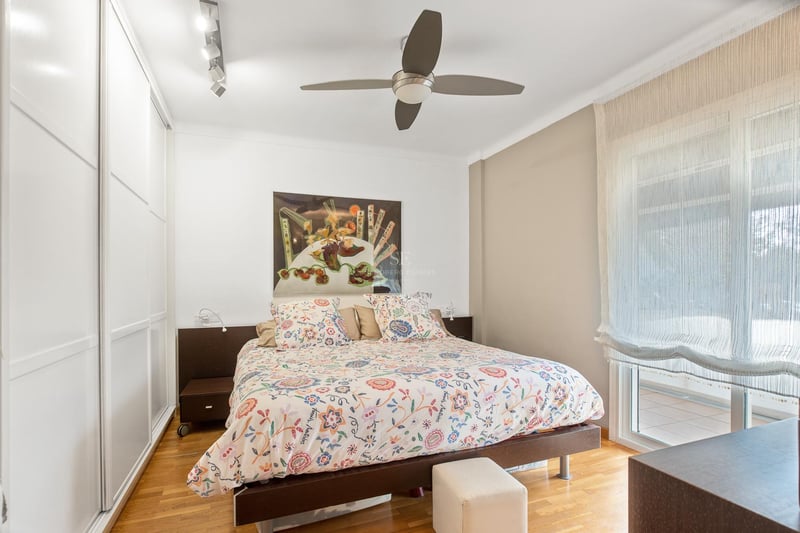 Chambre avec parquet en chêne, placards intégrés blancs, lit double et porte vitrée donnant sur terrasse.