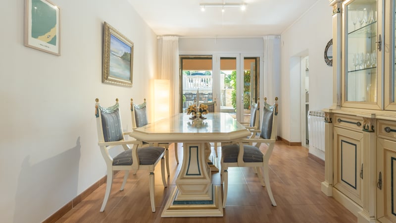 Salle à manger lumineuse avec table et chaises ornées crème et bleu, vitrine assortie et vue sur la terrasse.