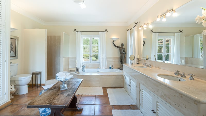 Large bathroom featuring a double marble vanity, built-in tub by the window, and traditional terracotta tile flooring.