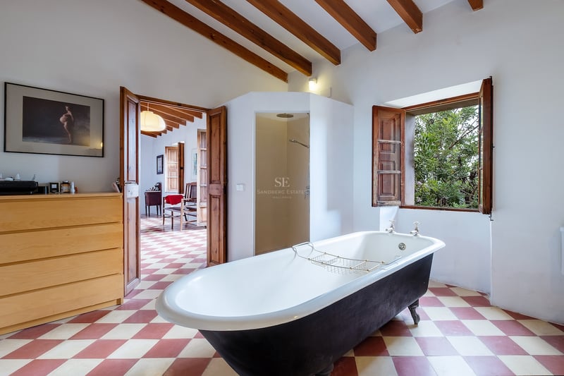 Salle de bain spacieuse avec baignoire îlot noire, poutres en bois apparentes, sol à damier et vue sur le jardin.