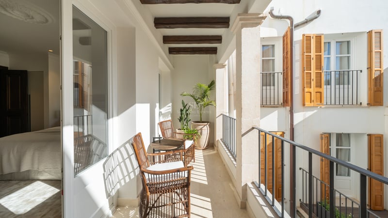 Sun-drenched private terrace with wicker seating, exposed wooden beams, stone pillars, and traditional wooden shutters.