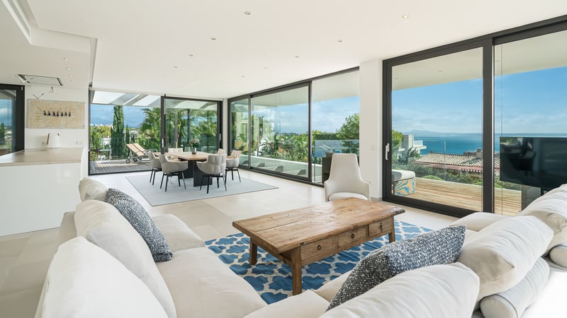 Salon spacieux avec canapés blancs, table basse en bois et grandes baies vitrées s'ouvrant sur une terrasse vue mer.