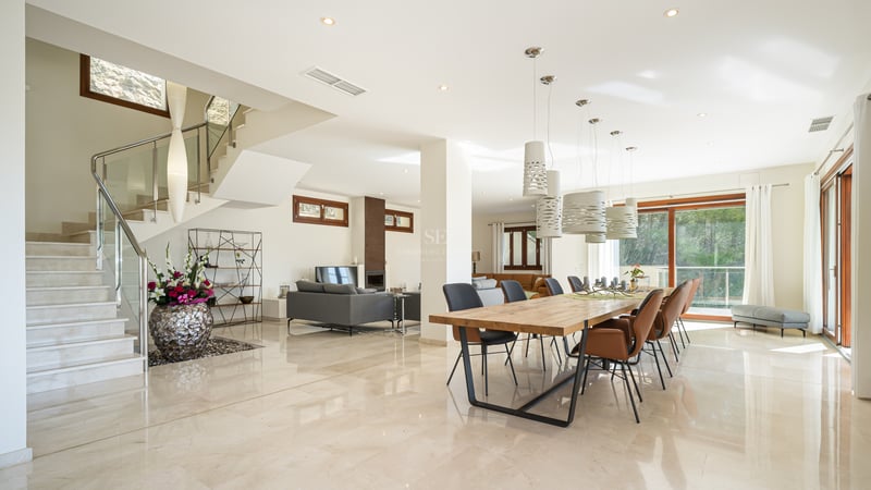 Salle à manger moderne à plan ouvert avec sol en marbre, grande table en bois, luminaires design et escalier en pierre.