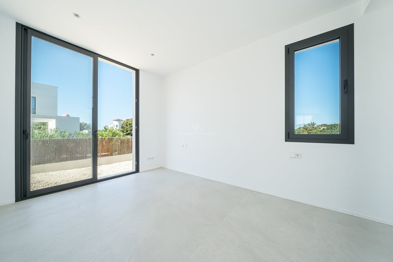 Pièce moderne vide avec murs blancs, sol en carrelage gris et une grande porte vitrée coulissante.
