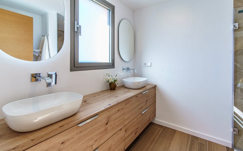 Salle de bain moderne avec un long meuble en bois, deux vasques blanches et des miroirs circulaires rétroéclairés.