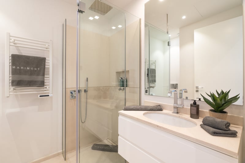 Salle de bain moderne comprenant une douche à l'italienne vitrée, un meuble vasque blanc et un sèche-serviettes.