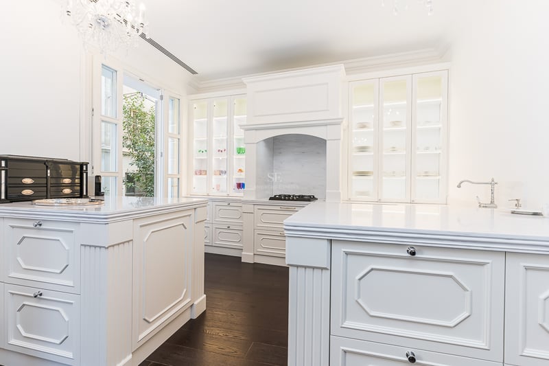 Cuisine élégante avec placards blancs, plans de travail en marbre, îlot central et lustre en cristal.