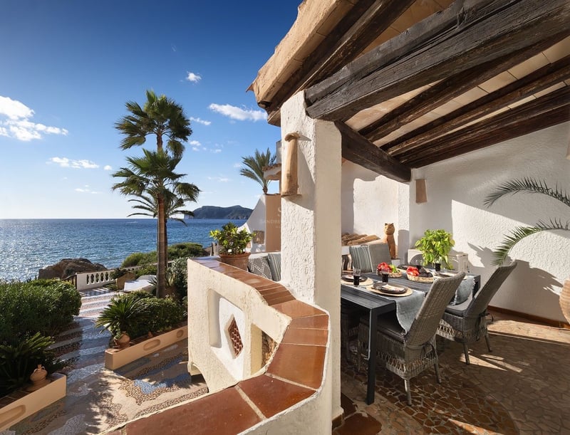 Terrasse couverte avec poutres en bois, table à manger, chaises en osier et vue imprenable sur la mer et les palmiers.