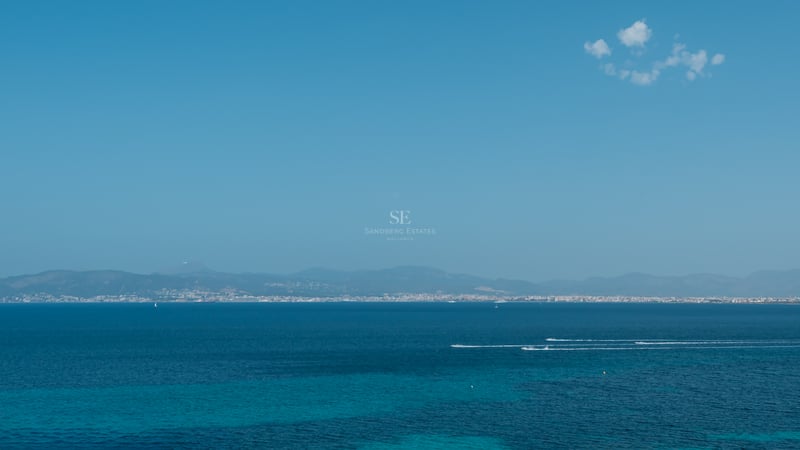 Vue grand angle de la mer Méditerranée turquoise avec le littoral et les montagnes au loin sous un ciel bleu clair.