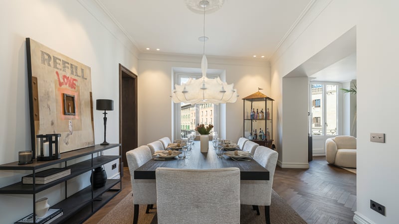 Contemporary dining room with dark wood table, upholstered chairs, designer chandelier, and oak herringbone floors.