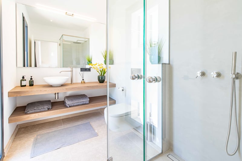 Bright minimalist bathroom featuring a glass walk-in shower, oak shelves, white vessel sink, and wall-hung toilet.