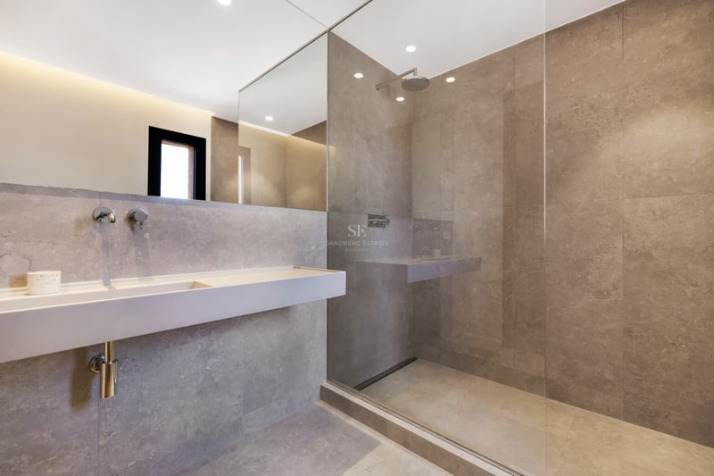 Salle de bain minimaliste avec carrelage gris, douche vitrée, lavabo suspendu et grand miroir.