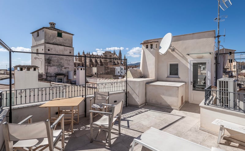 Toit-terrasse spacieux avec mobilier en bois et vue imprenable sur la cathédrale historique sous un ciel bleu.